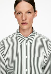 Striped button-up shirt featuring vertical green and white stripes, a pointed collar, and a chest pocket with contrasting stitching.