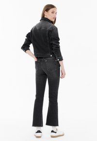 Black denim jacket with matching flared jeans. Features minimal stitching, raw hems, and back pockets. Worn with casual white sneakers.