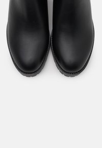 Stivali ankle in pelle nera con finitura liscia, punta arrotondata e suola in gomma texturizzata. I dettagli cuciti lungo il bordo aggiungono dimensione.