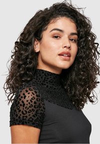 Svart topp med høy hals og korte gjennomsiktige ermer med svart leopardmønster. Glatt tekstur med en tettsittende design.