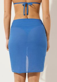 Falda midi de punto azul con cintura ajustada, hecha de un tejido ligero. Acabado texturizado y transparente con un borde liso en el dobladillo.
