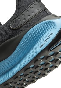 Gros plan de la semelle noire et bleue de la sneaker Nike ReactX montrant une adhérence texturée et une sangle latérale avec des détails circulaires.