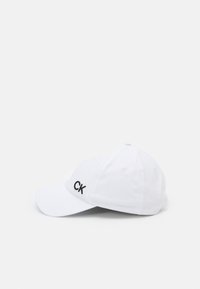 Căciulă albă cu brăcină curbă, are logo-ul brodat negru "CK" pe față, fabricată din material neted, cu șase orificii de ventilație.