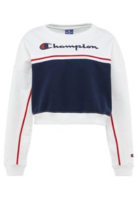 Sudadera blanca recortada con panel azul marino, rayas rojas y blancas, y el logo de "Champion" en azul oscuro. Material suave de mezcla de algodón.