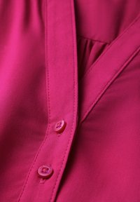 Fuchsia button-up blouse with a smooth texture, featuring pink buttons and a pleated design along the front panel.
