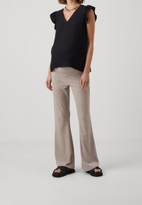 Musta, teksturoitu yläosa, jossa röyhelöhihat, yhdistetty vaaleabeigeihin, istuviin ja liehuviin housuihin. Malli käyttää mustia sandaloita, joissa on paksu pohja.