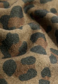 Leoparda raksta audums brūnās un melnās nokrāsās, ar teksturētu virsmu, kas satur noapaļotus, neregulārus plankumus uz mīksta, nedaudz spīdīga pamata.