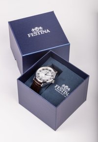 Festina pulksteņi zila kastē; sudraba ciparnīca ar melniem cipariem, brūna ādas siksniņa, metāla korpuss un zīmola logo uz iepakojuma.