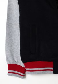 Marineblauwe en grijze sweatshirt met een ribgebreide manchette in rood en grijs, een effen marineblauwe body en een zijzak met een nette afwerking.