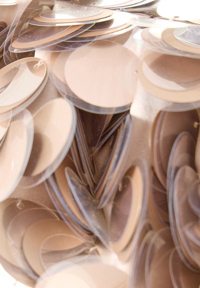 Στρωματοποιημένοι διαφανείς και αδιαφανείς μπεζ κυκλικοί δίσκοι που επικαλύπτονται, δημιουργώντας ένα υφασμένο και αντανακλαστικό μοτίβο σε ουδέτερους τόνους.