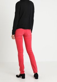 Jean rouge slim avec poches, associé à un haut noir à manches longues. La tenue est complétée par des chaussures noires à talons.