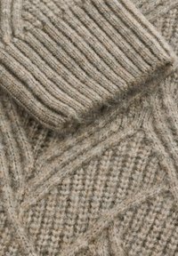 Beżowy sweter z dzianiny z detalami, które przedstawiają teksturowany prążek z wyraźnymi ukośnymi akcentami, eksponujący grube, miękkie włókna wełniane.