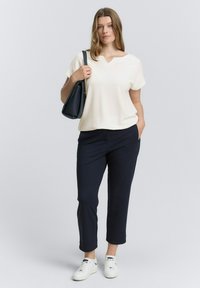 Witte textuur korte mouw top met een V-hals, gecombineerd met donkerblauwe tailored broek en witte sneakers, met een zwarte schoudertas.