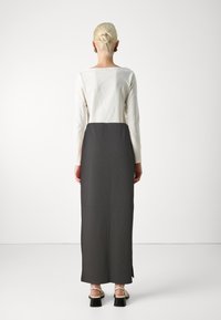 Lang kleed met een witte top en een donkergrijs, geplooid rok. Het heeft een ronde halslijn en zijsplitten, gecombineerd met sandalen met banden.