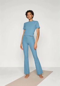 Nais peab paljajalu joogamatil, seljas helesinine ühte tonni lühikeste varrukatega topp ja laiad püksid.