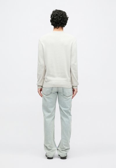 Pull gris clair avec un col et un ourlet côtelés, associé à un jean bleu clair ample avec des poches arrière et des coutures discrètes.