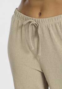 Pantalons de survêtement en tricot beige avec une taille élastique et un cordon de serrage. Tissu texturé, ajusté à la taille, montrant un gros plan de la partie supérieure.