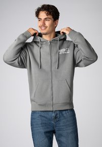 Gray zip-up hoodie with a front pocket, drawstrings, and printed text. Soft fabric, relaxed fit, and ribbed cuffs and hem.