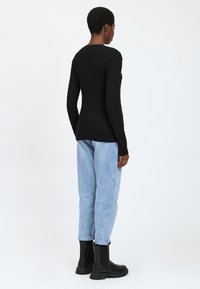Maglione nero a costine con maniche lunghe e scollatura rotonda, indossato con jeans azzurri a vestibilità rilassata e stivali neri alla caviglia.