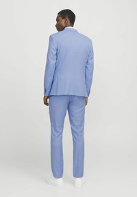 Light blue suit made of fabric with a smooth texture, featuring a tailored fit and matching trousers, paired with white sneakers.