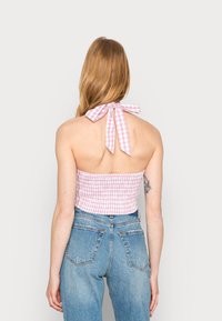 Top de alças de algodão em padrão de xadrez rosa e branco, com design franzido na cintura e fecho em laço nas costas. Combinado com jeans de denim.
