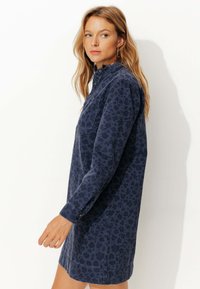 Robe chemise en denim bleu marine avec un subtil imprimé léopard, col boutonné, manches longues et une poche poitrine. Texture lisse.