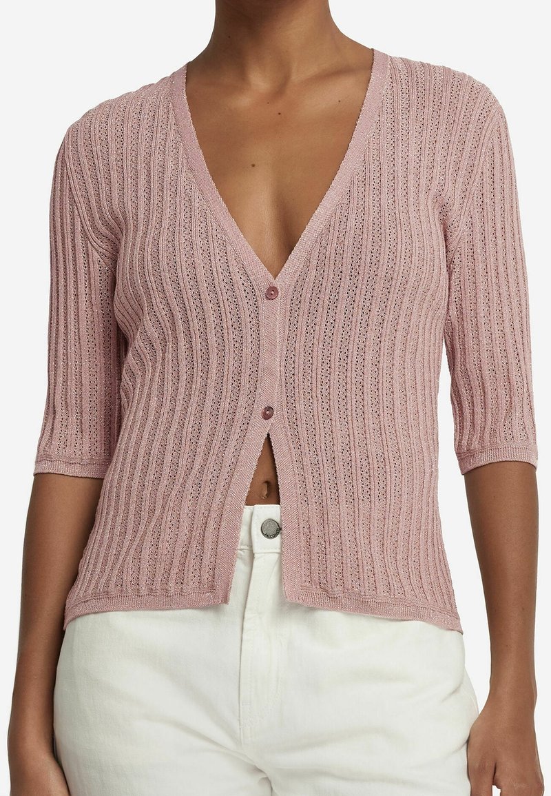 Pink knitted cardigan featuring a deep V-neck, ribbed texture, short sleeves, and a button closure in the center. Worn with white pants.