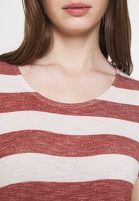 Camiseta a rayas rojas y blancas con un escote en forma de barco y textura acanalada. Las rayas varían en ancho, creando un patrón ondulado.