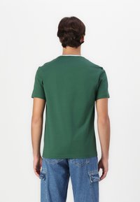 Tricou scurt cu mânecă scurtă de culoare verde închis, cu guler rotund având un accent deschis, fabricat din bumbac. Purtați-l cu blugi cargo de culoare bleu deschis, având un design simplu.