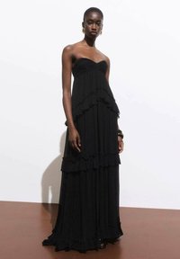 Black strapless maxi dress with layered ruffles, soft texture, and flowing silhouette. Features a fitted bodice and relaxed skirt design.