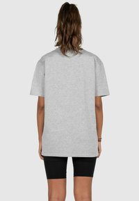 Grå oversized t-shirt lavet af blødt stof, med korte ærmer og afslappet pasform. Bagud vises et ensfarvet design uden mønstre.