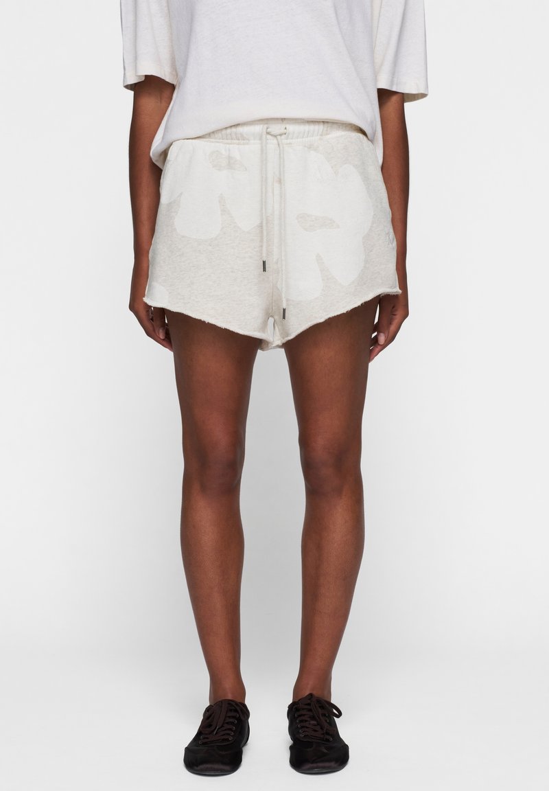 Helle, graue Shorts aus weichem Stoff, mit einem weißen Blumenmuster, Kordelzugbund und fransigem Saum. Kombiniert mit dunklen Schuhen.