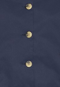 Tamsiai mėlynas audinys su trimis auksiniais mygtukais, lygiu paviršiumi ir minimalistiniu dizainu, pabrėžiant mygtukų išdėstymą ir siuvimo detalę.