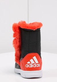 Czarne botki za kostkę z czerwonym sztucznym futrem, z wyściółką z gąbki, wyraźnym białym logo adidas i białą gumową podeszwą.