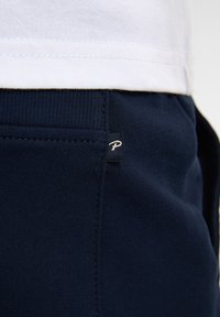 Navyblauwe zachte joggers van stof met een wit logolabel op de zak, een geribde tailleband en een gladde textuur.