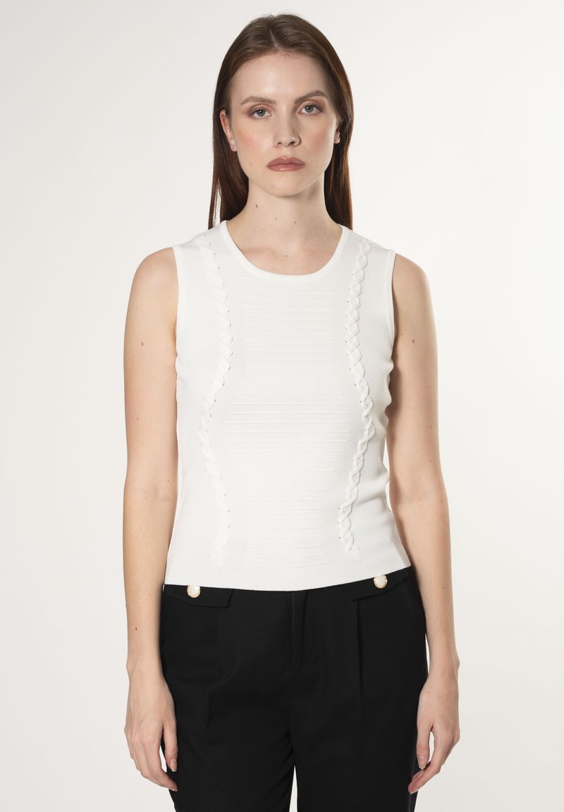Top blanco sin mangas con acentos texturizados y ondulados en los lados, con un escote redondo y un diseño ajustado. Combinado con pantalones negros.