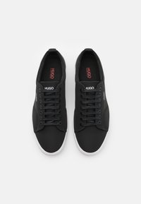 Czarne sneakersy z gładką tekstylną cholewką, z białą gumową podeszwą, czarnymi sznurowadłami i czerwonym detalem logo na wkładce.