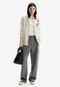 Camicia a righe con design floreale, canotta bianca, pantaloni grigi a gamba larga e borsa nera con motivo. Sneakers con suola testurizzata.