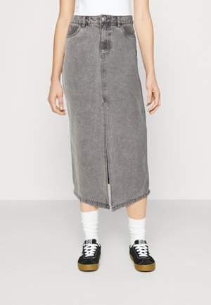 Grijze spijkerrok van middellange lengte met een voorsplit, gedragen met witte sokken en zwarte sneakers door een staande persoon.