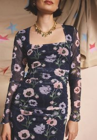 Gėlėta ilgarankovė suknelė tamsiai mėlynos spalvos su rožiniais ir žaliais gėlių raštais. Lygi medžiaga, kvadratinis iškirptės kaklas ir laikančioji figūrą forma. Auksinė grandinėlė.