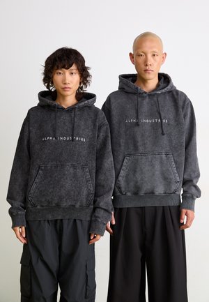 Hættetrøjer i falmet mørkegrå med frontlommer, prydet med "ALPHA INDUSTRIES" logo. Blødt stof med ribbede manchetter og kant.