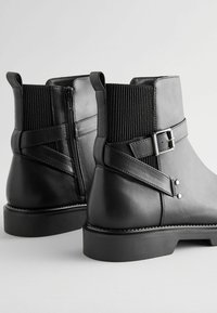 Mustad nahast ankle saapad elastsete külgseinadega, niidist detailidega ja tekstureeritud disainiga. Sile pealmine osa koos lamedate kummiga talladega.