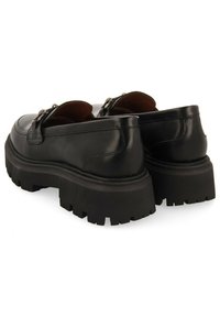 Chaussures en cuir noir avec une semelle en caoutchouc épaisse et texturée. Équipées d'un bout rond et d'une boucle décorative sur la partie supérieure.