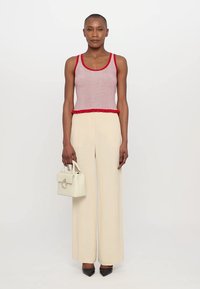 Débardeur rayé rouge et blanc avec un ourlet volanté, associé à un pantalon large crème. Le mannequin tient un petit sac à main blanc et porte des escarpins noirs à talons pointus.