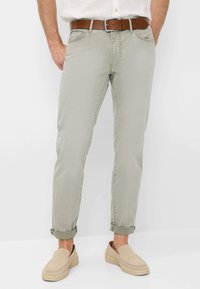 Pantaloni grigi chiari a sigaretta con una leggera texture, orli arrotolati e una cintura in pelle marrone. La calzatura presenta scarpe beige slip-on.