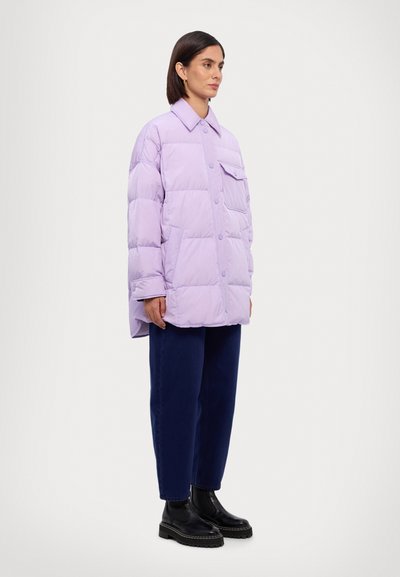 Lila pufferjack met een boxy snit, grote knopen, zakken en een platte kraag, gecombineerd met donkerblauwe broek en zwarte platformlaarzen.