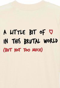 Cremefarvet t-shirt med korte ærmer, der har fed sort tekst og en rød hjerteillustration. Teksten lyder: "En smule ♥ i denne brutale verden (men ikke for meget)."