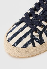 Baskets en toile avec motif rayé bleu marine et blanc, bout rond et semelle en jute tissée. Comprend un design à lacets et des œillets en métal.