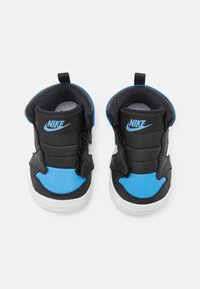 Schwarz-blaue Nike-Sneaker mit gepolstertem Kragen, Klettverschlüssen und weißen Gummisohlen. Das Material wirkt synthetisch und strukturiert.