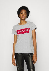 Grå kortærmet t-shirt med et rødt Levi's-logo i klassisk design, lavet af bomuld med en glat tekstur. Sammen med sorte læderbukser.